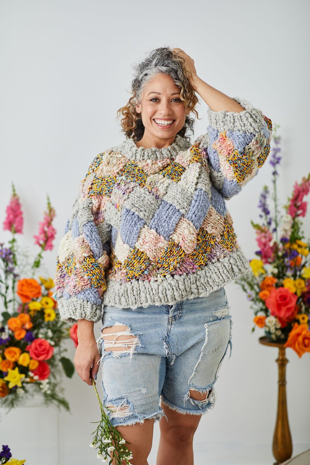 Model smiling with hand on head wearing entrelac sweater.