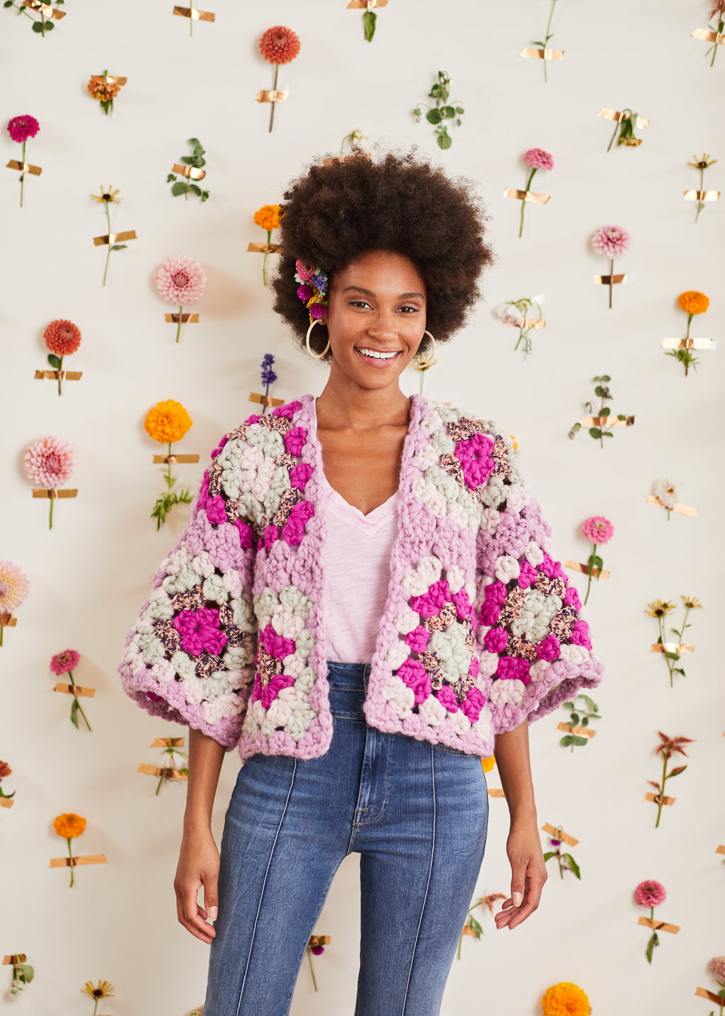 Model smiling in front of flower wall wearing granny square cardi