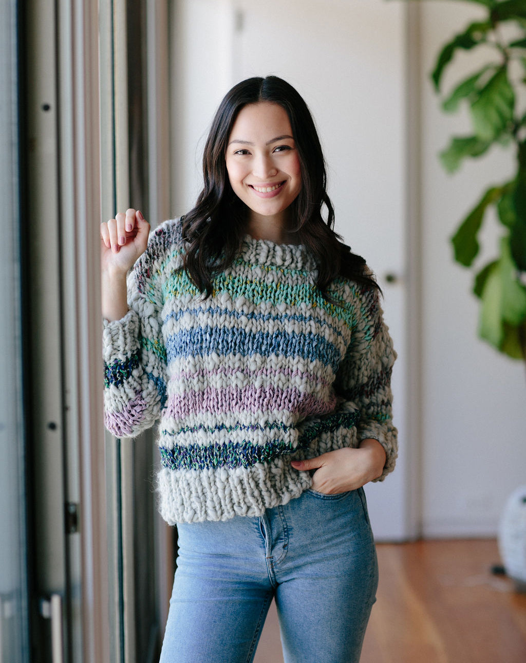 Model holding one arm up and hand in pocket wearing striped sweater.