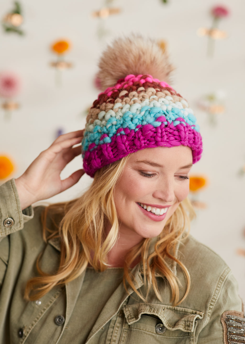 Smiling modeling with hand on a knitted hat.