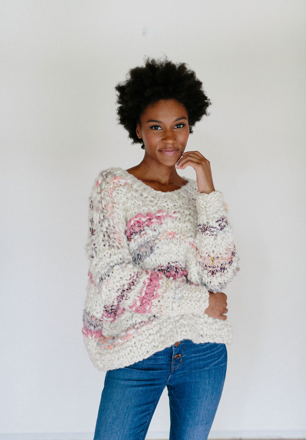 Model with hand on face wearing sweater.